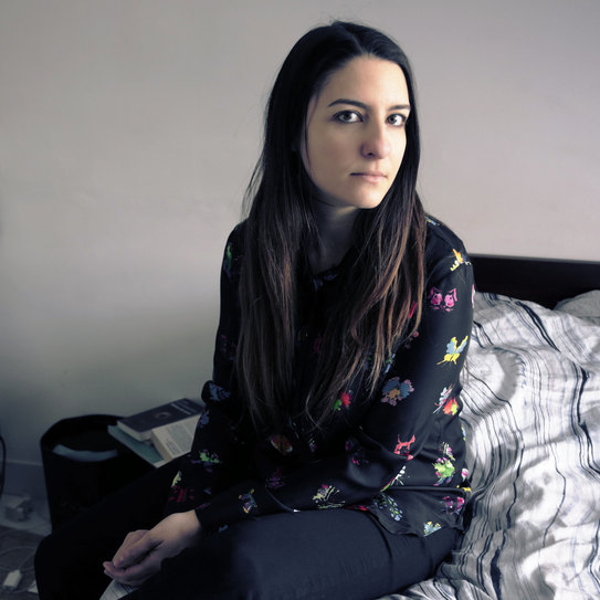 Das Foto zeigt die Autorin Alexandra Badea auf einem ungemachten Bett sitzend. 