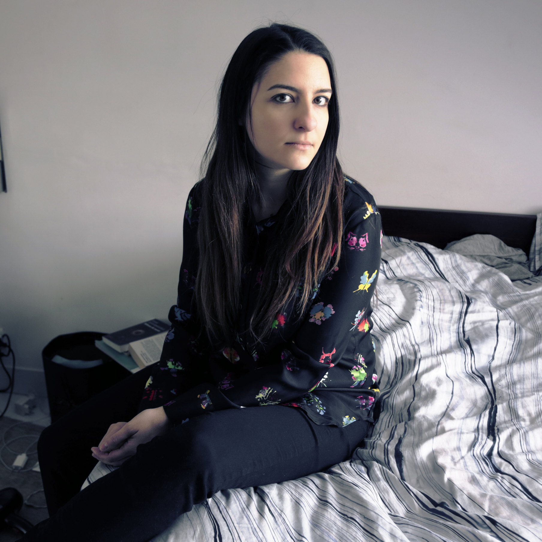 Das Foto zeigt die Autorin Alexandra Badea auf einem ungemachten Bett sitzend. 